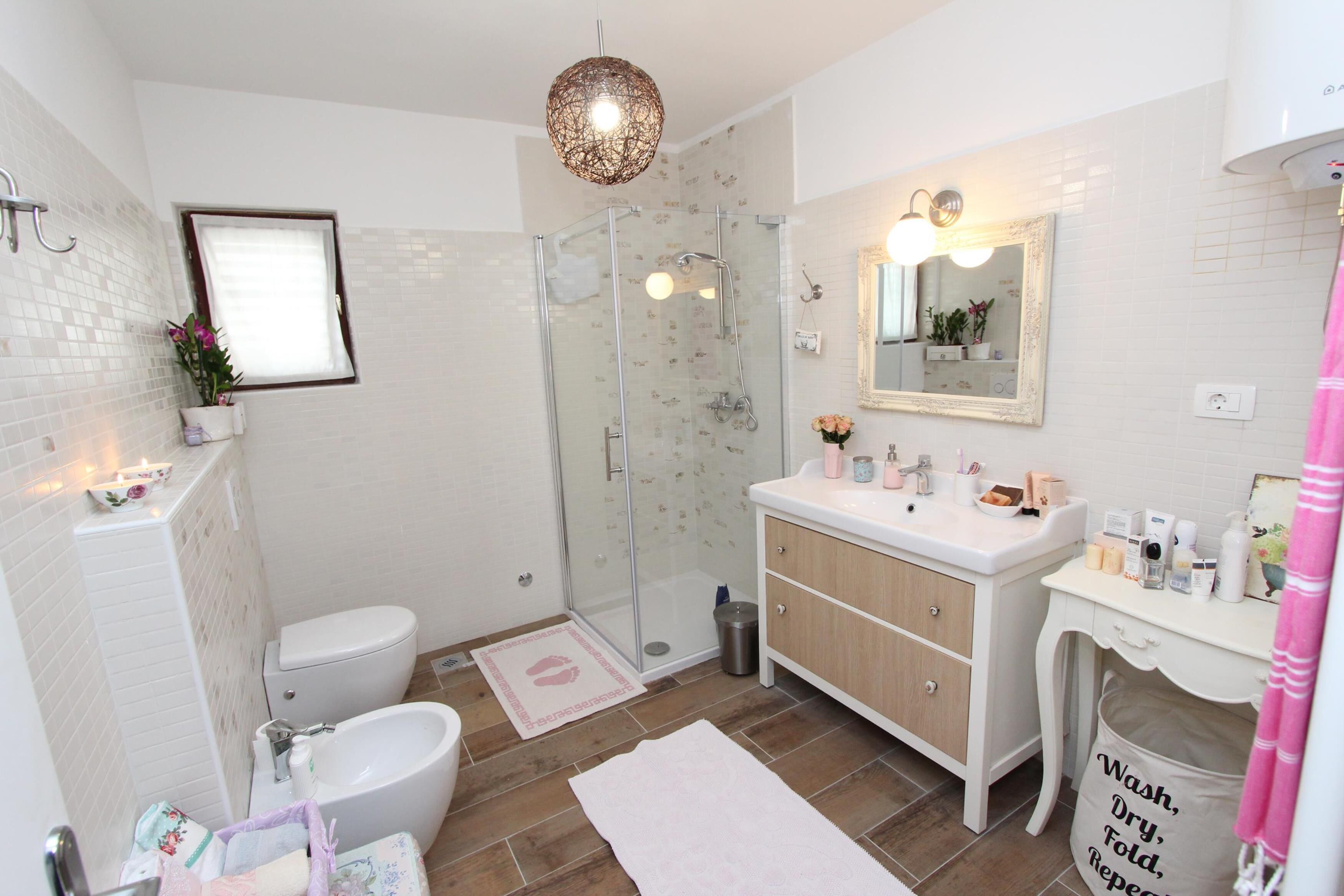 A modern bathroom with a glass shower, white tiles, a vanity with a mirror, and a sink with toiletries.
