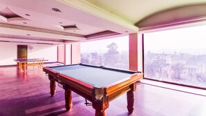 Una mesa de billar en una habitación con ventanas amplias y vistas a un paisaje urbano.