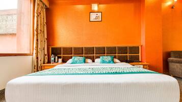 Une chambre d’hôtel avec un grand lit, une tête de lit ornée d’un panneau décoratif, une table de chevet avec une lampe et une fenêtre avec des rideaux.