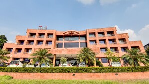 Un hotel de varios pisos con un atrio central, palmeras y coches aparcados en la entrada.
