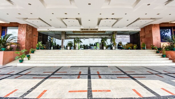 Una entrada imponente con una escalera de mármol que conduce a una zona de recepción, rodeada de plantas en macetas y arquitectura moderna.