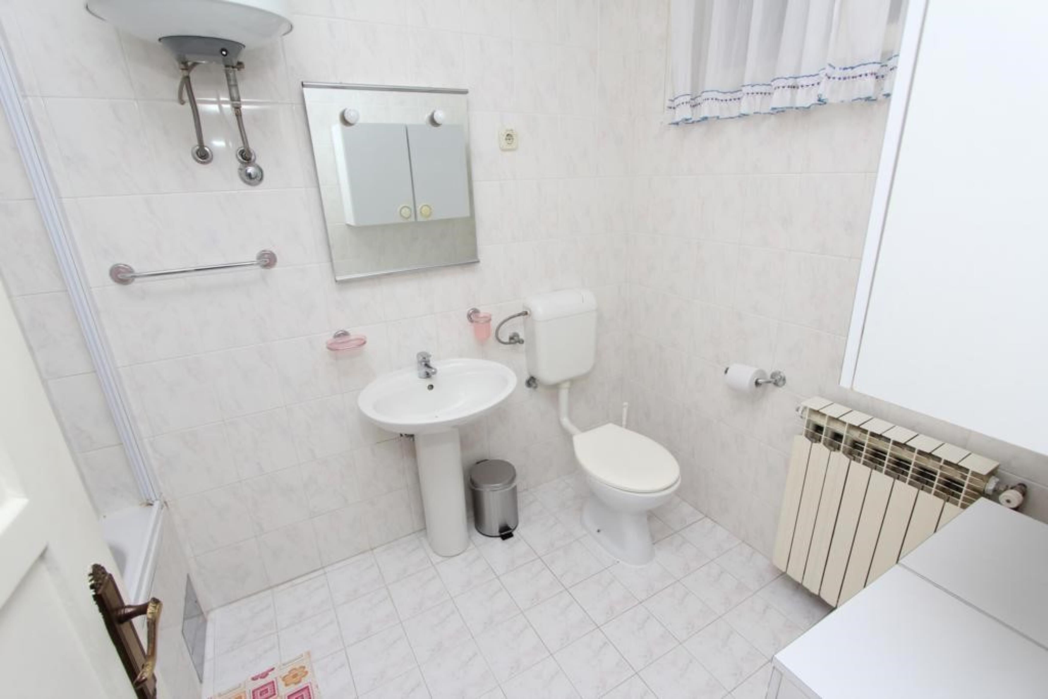 Un baño con inodoro, lavabo, espejo, toallero y radiador.