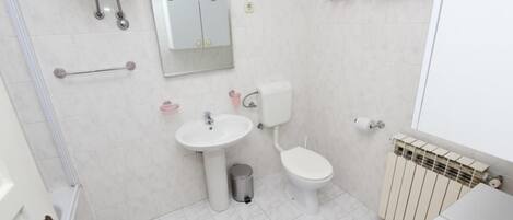 Un baño con inodoro, lavabo, espejo, toallero y radiador.