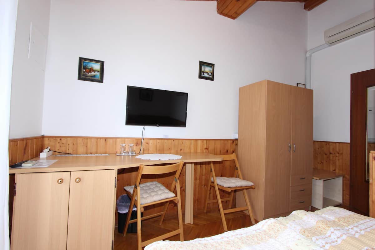 Un dormitorio con una cama, un escritorio, dos sillas, un armario y un televisor en la pared.