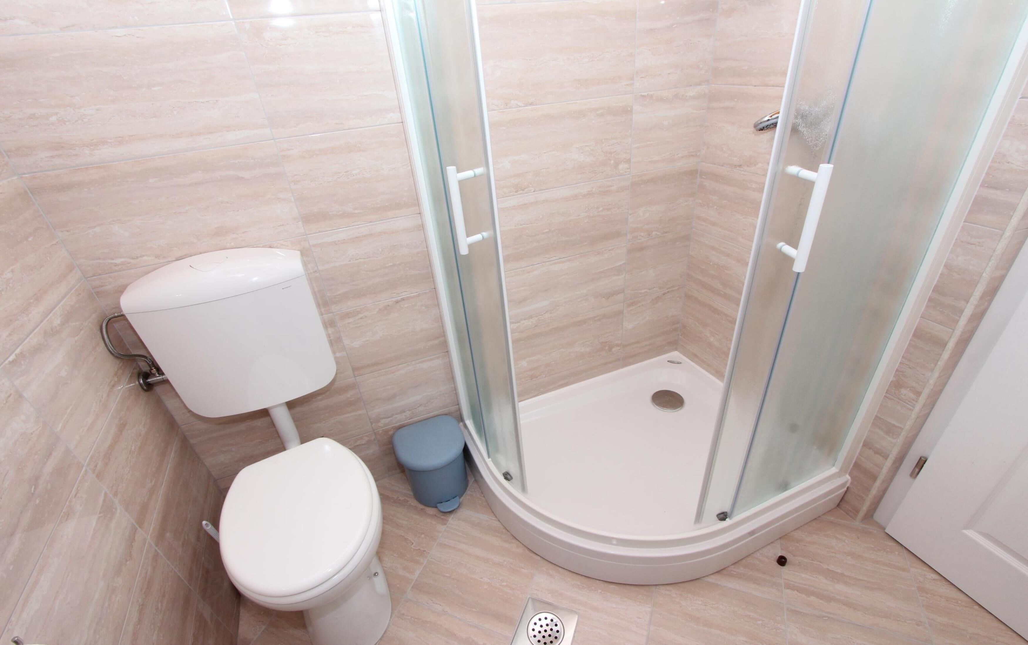 A modern bathroom with a toilet, a shower with glass doors, and a blue trash bin.