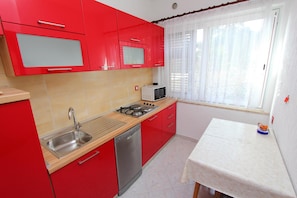 A kitchen with red cabinets, a stainless steel sink, a microwave, and a gas stove. - Apartments Aurora (Rovinj)