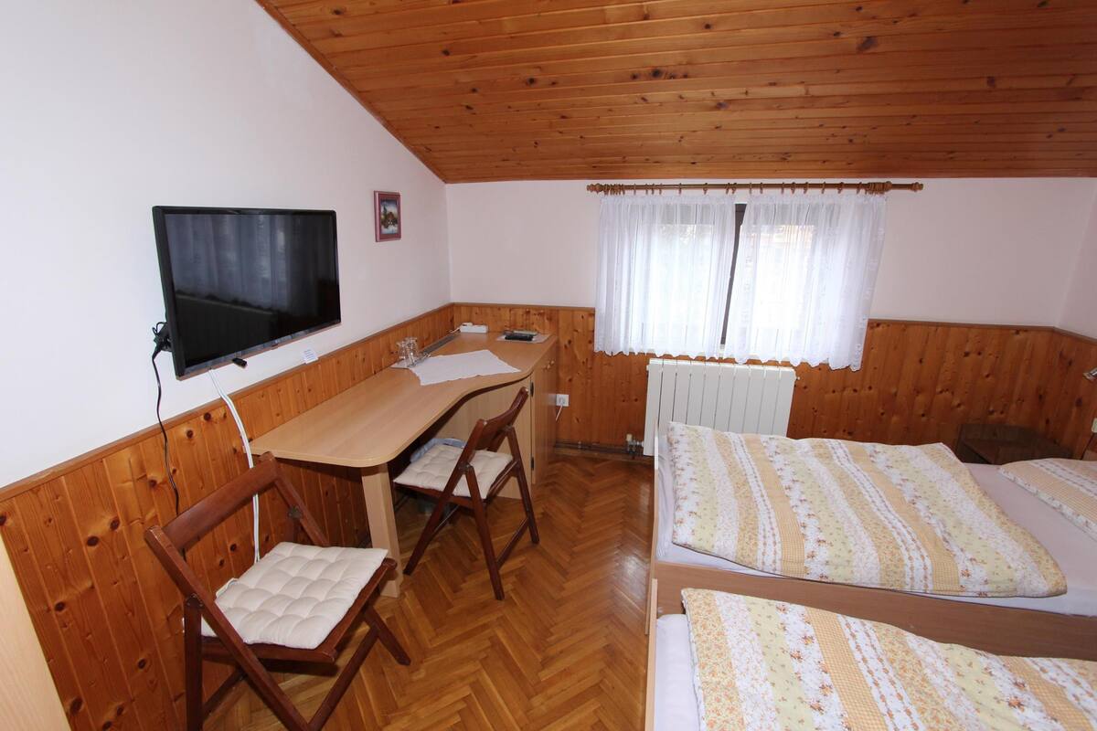 Una habitación con techo de madera, una cama con ropa de cama floral, un escritorio de madera con una silla y un televisor montado en la pared.
