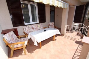 An outdoor patio with a table and two chairs, a window with shutters, and a metal railing.