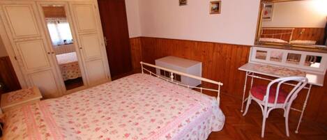 Un dormitorio con cama, escritorio, silla, cómoda y espejo.