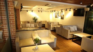 Un espacio lounge moderno con varios sofás y mesas, una pared de ladrillo y un televisor montado.