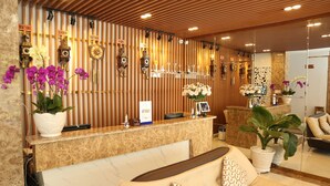 Una zona de recepción con mostrador de mármol, un sofá con cojines estampados y una pared decorada con relojes y orquídeas.