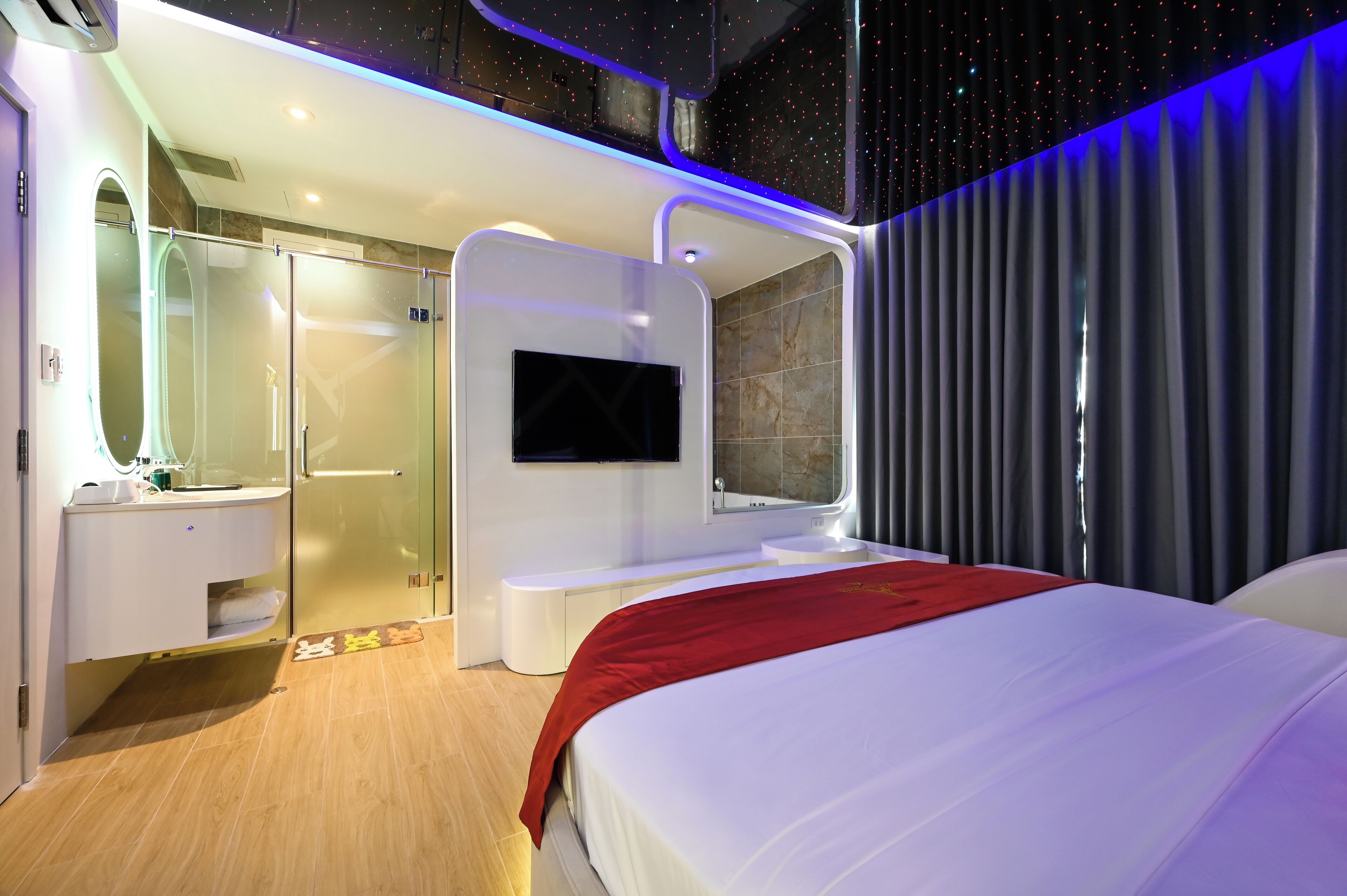 A modern hotel room with a large bed, a TV mounted on the wall, a shower area, and a vanity with a mirror.