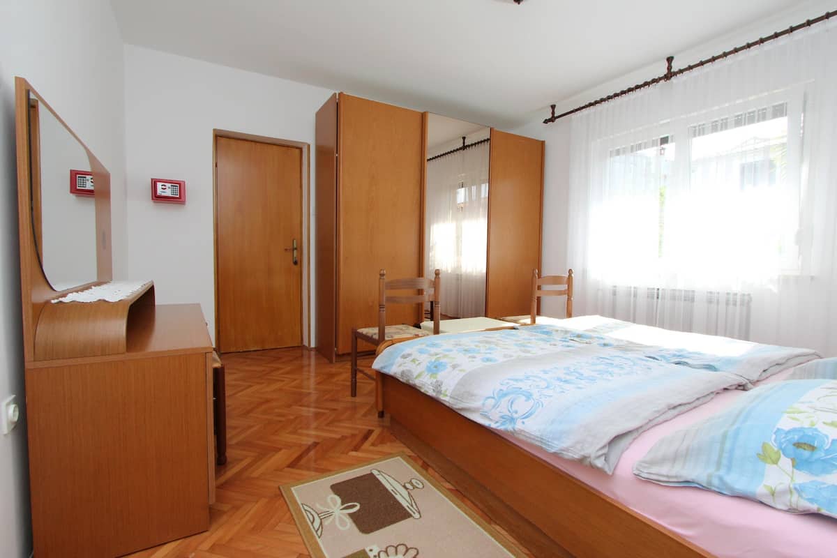 A bedroom with a wooden bed, a chair, a wardrobe, and a mirror.