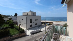 A modern building with a flat roof, a balcony with a striped awning, and a view of the sea. - Rooms and Apartments Bella Vista (Rovinj)