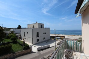 En modern byggnad med ett platt tak, en balkong med en randig markis och utsikt över havet.