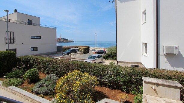 A residential building with a view of the sea, parked cars, and a garden with yellow flowers. - Rooms and Apartments Bella Vista (Rovinj)