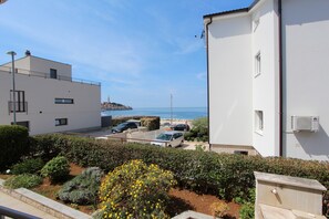 Un immeuble résidentiel avec vue sur la mer, des voitures garées et un jardin parsemé de fleurs jaunes.