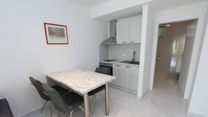 A modern kitchen with white cabinets, a marble countertop, and a dining area with a table and chairs. - Rooms and Apartments Bella Vista (Rovinj)