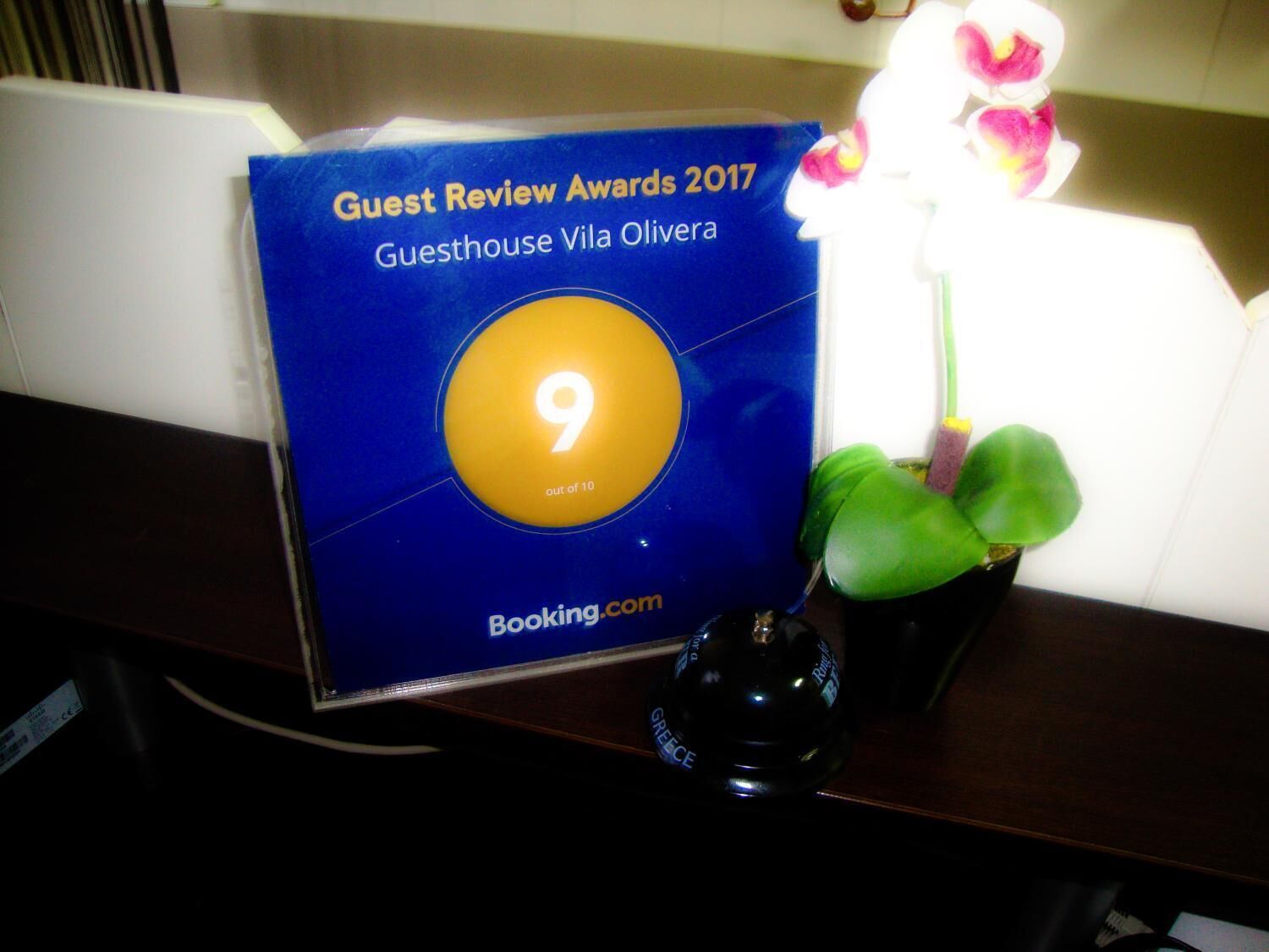 A blue award plaque with a 9 out of 10 rating for Guesthouse Vila Olivera, placed on a desk next to a potted plant.