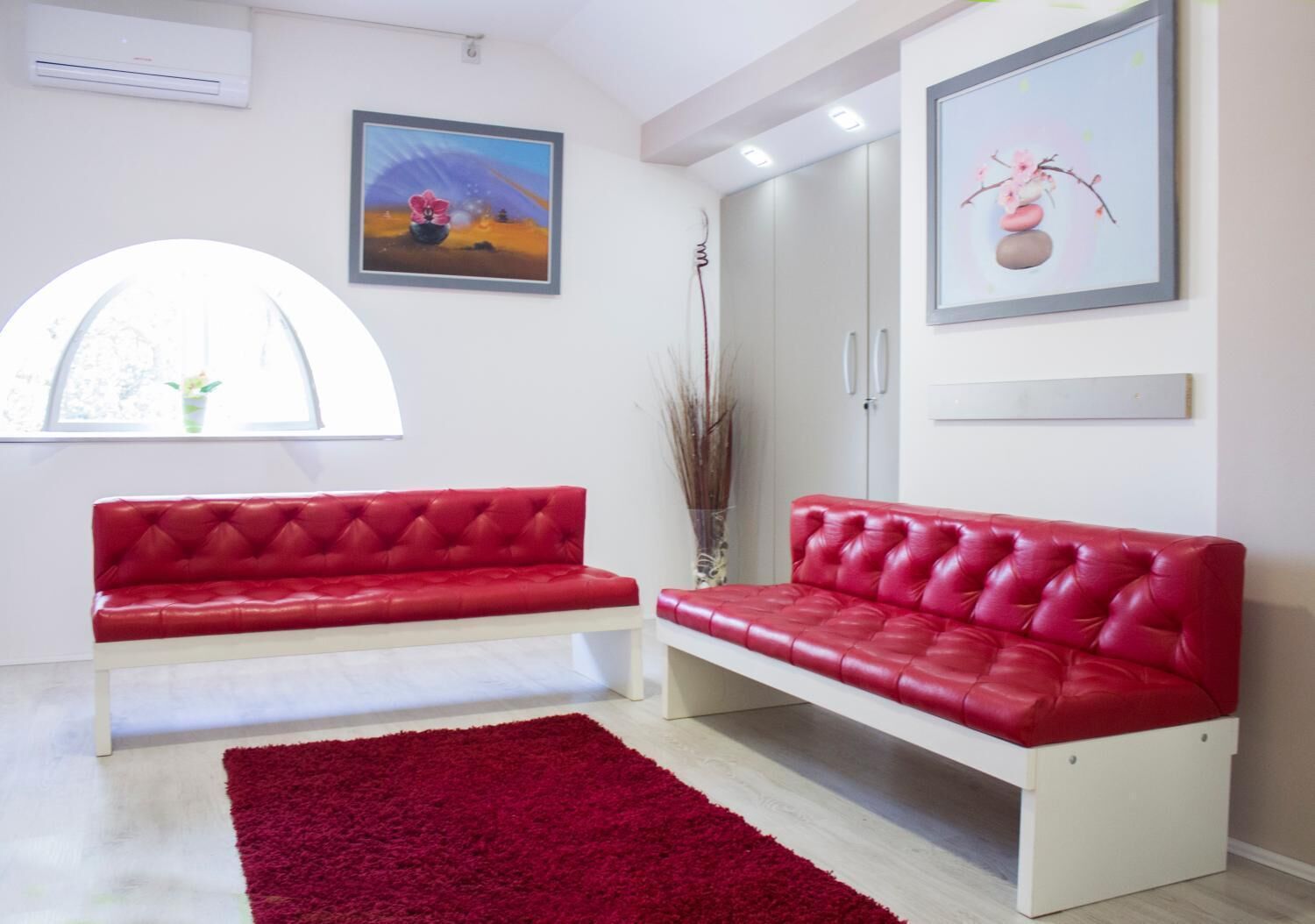 A modern living room with two red leather sofas, a red rug, and artwork on the walls.