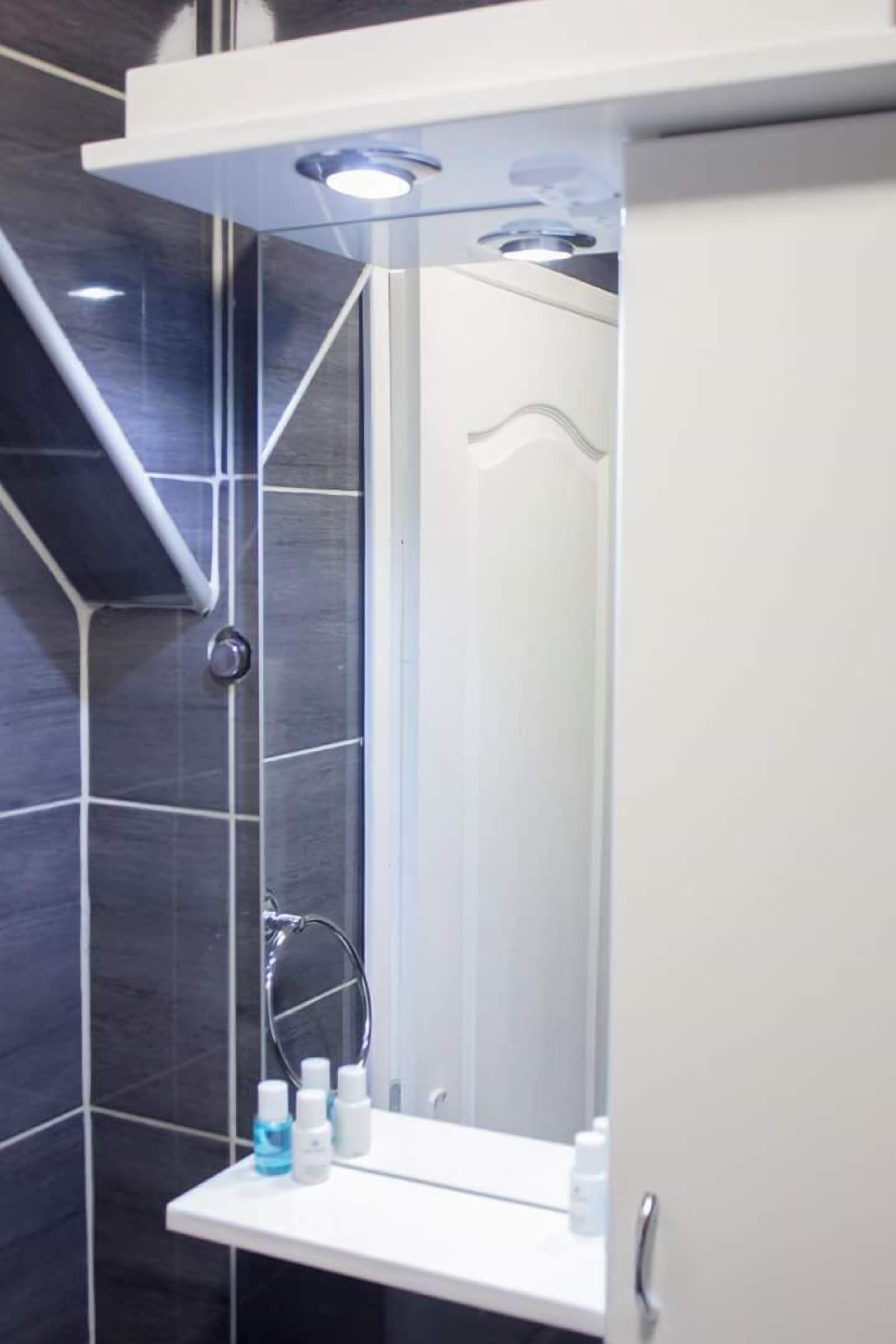 A modern bathroom with a shower, a white sink with toiletries, and a mirror.