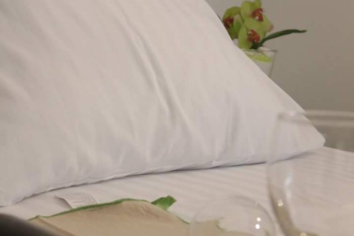 Una cama con sábanas blancas, una botella de vino y dos copas sobre una mesa.