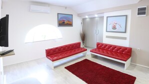 Een moderne woonkamer met twee rode banken, een rood vloerkleed, een televisie en kunstwerken aan de muur.