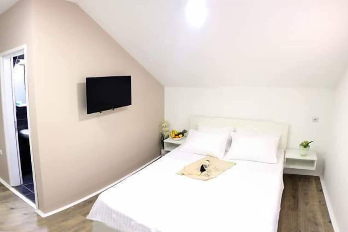 Un dormitorio con una cama, un televisor montado en la pared y una mesita de noche con una lámpara.