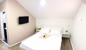 A bedroom with a bed, a TV mounted on the wall, and a bedside table with a lamp.