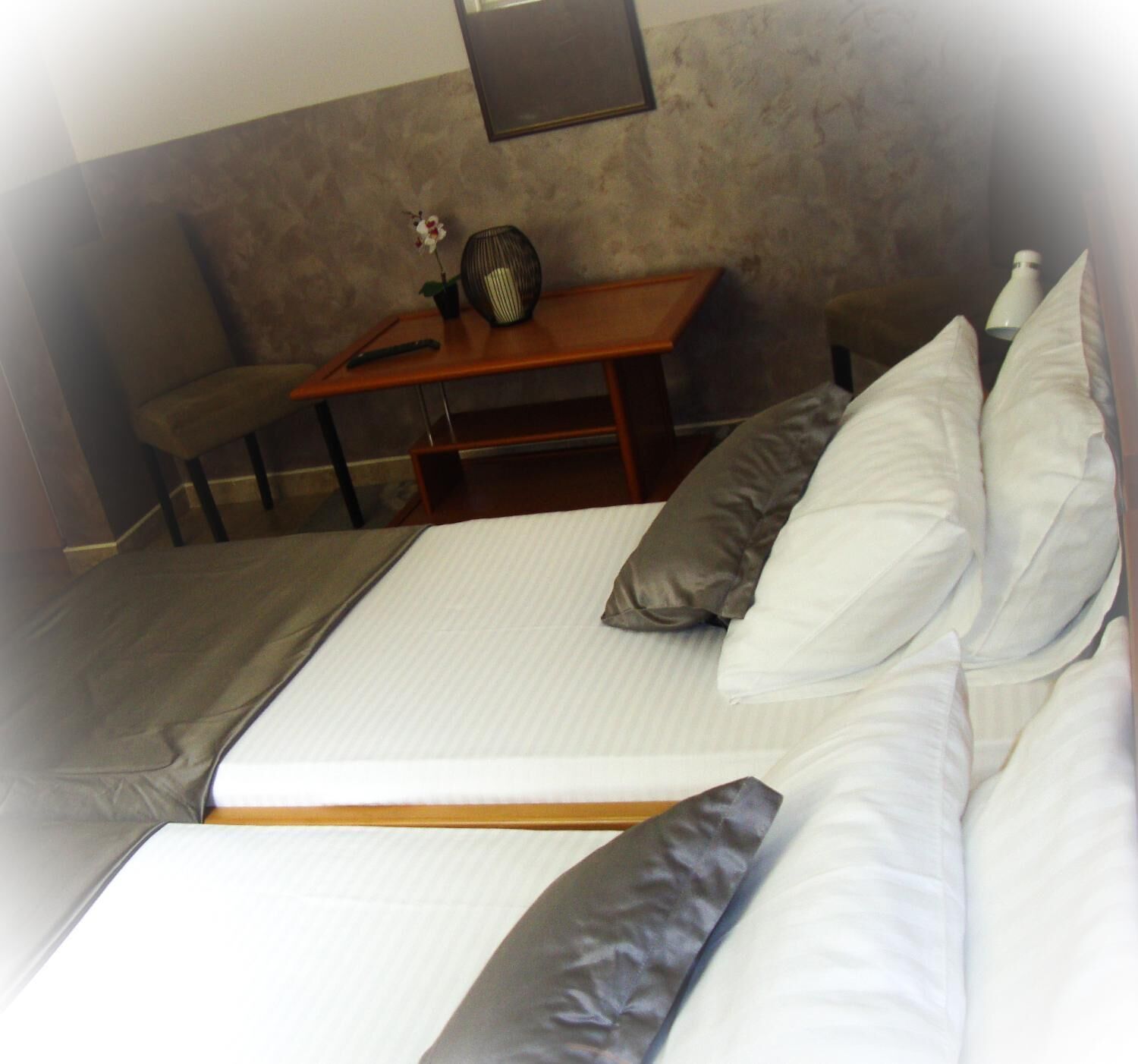 A single bed with a mattress, pillows, and a bedside table with a remote control and a flower vase.