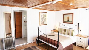 A bedroom with a wooden ceiling, a bed with a metal frame, a nightstand, a radiator, and a door leading to another room. - Sheephouse Manor (Maidenhead)