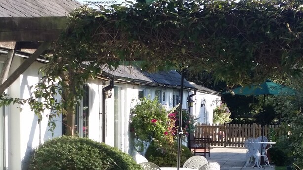 A garden area with a white table and chairs, a potted plant with flowers, and a wooden fence in the background. - Sheephouse Manor (Maidenhead)