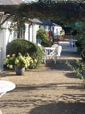 A garden area with a white table and chairs, a potted plant with flowers, and a wooden fence in the background.
