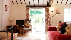 A living room with a wooden ceiling, a television on a wooden stand, a red sofa, and a chair with cushions. - Sheephouse Manor (Maidenhead)