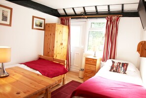 A bedroom with two beds, wooden furniture, a window with curtains, and a lamp. - Sheephouse Manor (Maidenhead)