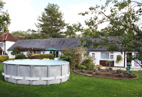 A residential area with a swimming pool, a house with a sloped roof, and a garden with various plants. - Sheephouse Manor (Maidenhead)