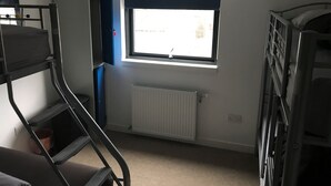 A dormitory room with bunk beds, a radiator, a window with blinds, and a desk. - An Cala Cafe and Bunkhouse - Hostel (Lochinver)