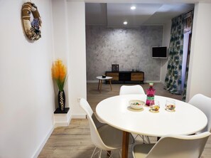 A dining area with a white table and chairs, a decorative wall hanging, and a vase with yellow flowers.
