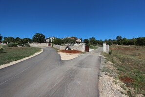 A residential street with a stone wall and a gated entrance leading to a house.
