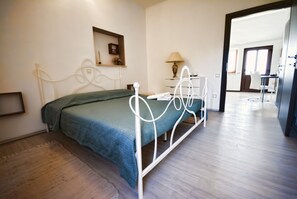 A bedroom with a bed, bedside table, lamp, and a view of another room.