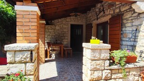 A stone-floored patio with a wooden table and chairs, a stone wall with a window, and potted plants. - Apartments with Shared Pool Bertetic (Kanfanar)