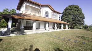 A two-story house with a covered porch, large windows, and a prominent tree in the background. - Cogent Holiday Home (Udunuwara)