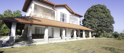 Una casa de dos pisos con un porche cubierto, ventanas amplias y un árbol destacado al fondo.