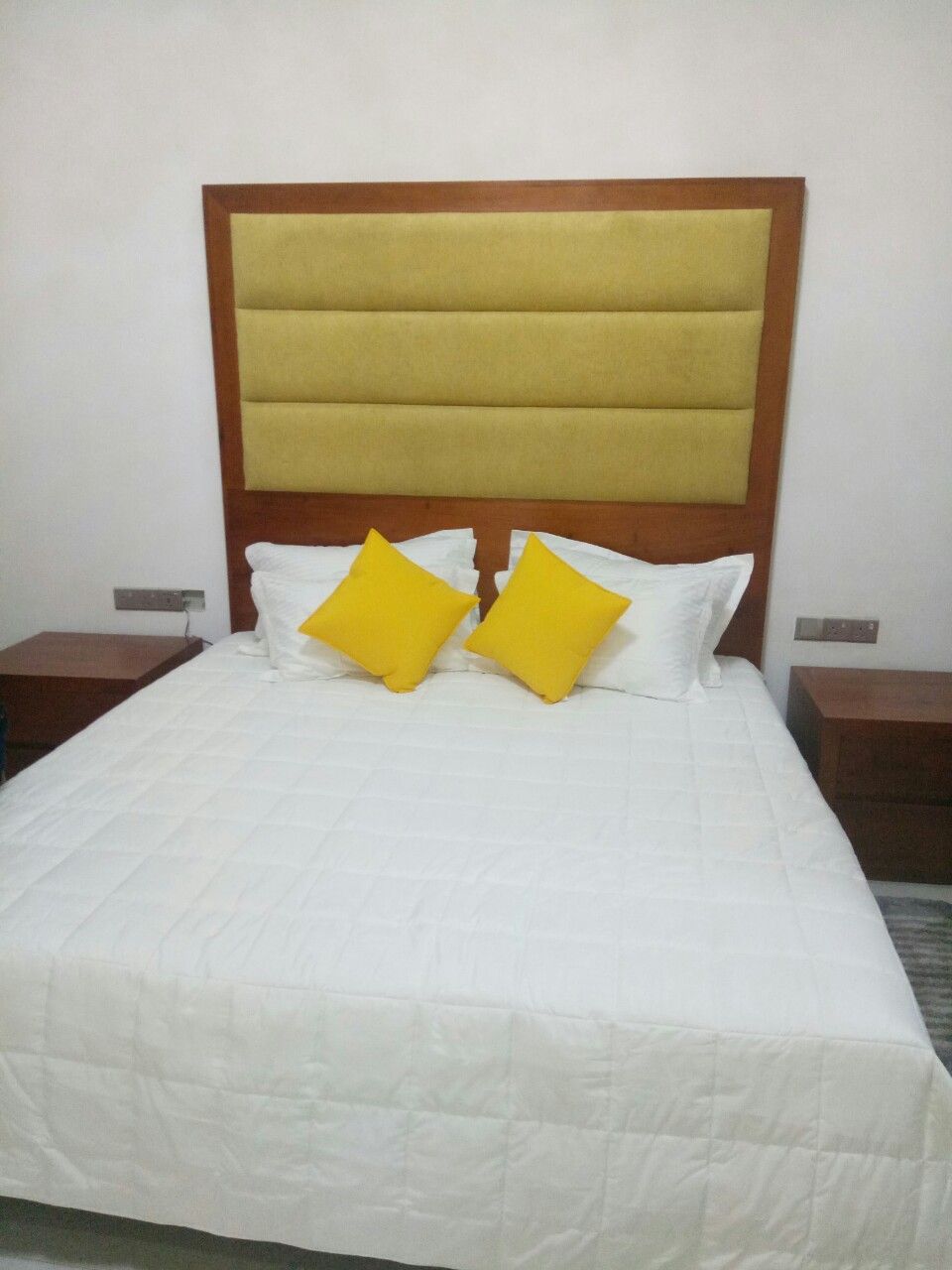 A hotel room with a large bed, a wooden headboard, two bedside tables, and a white bedspread.