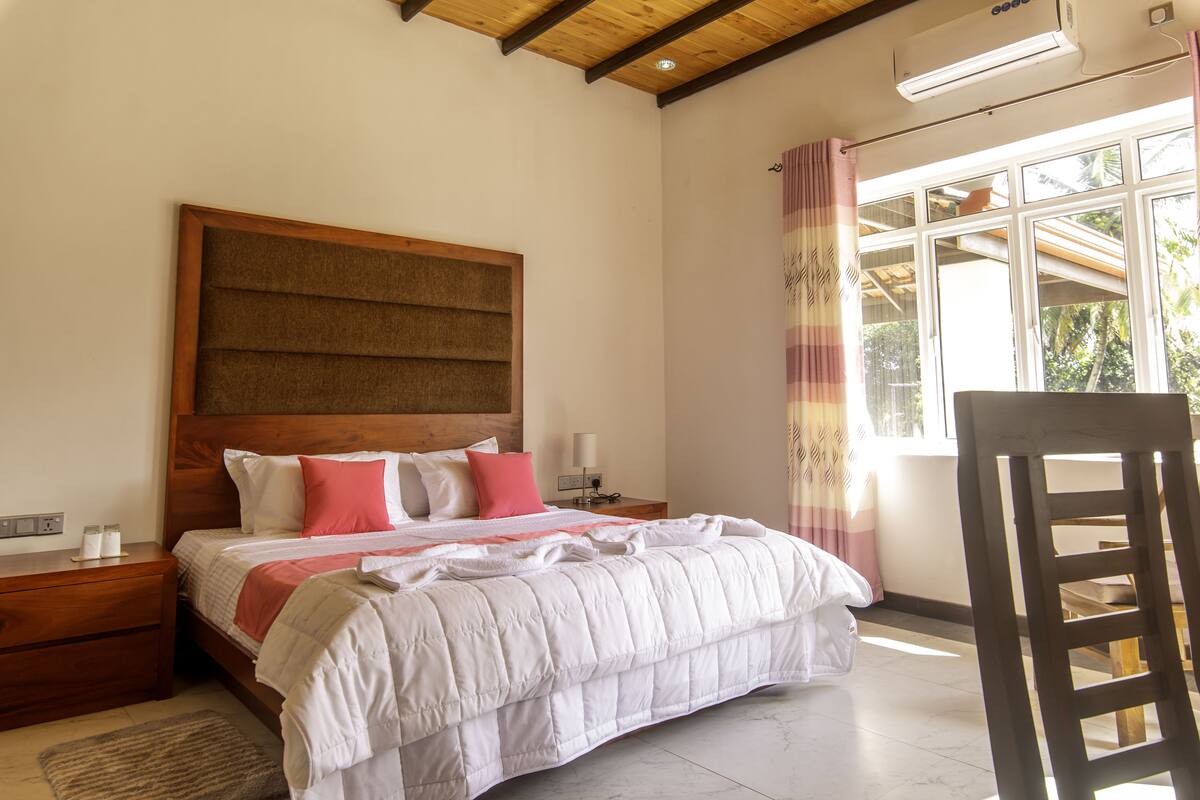 A bedroom with a large bed, wooden headboard, bedside tables, and a window with curtains.