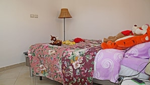 Un dormitorio con una colcha estampada con motivos florales, una lámpara y peluches en la cama.