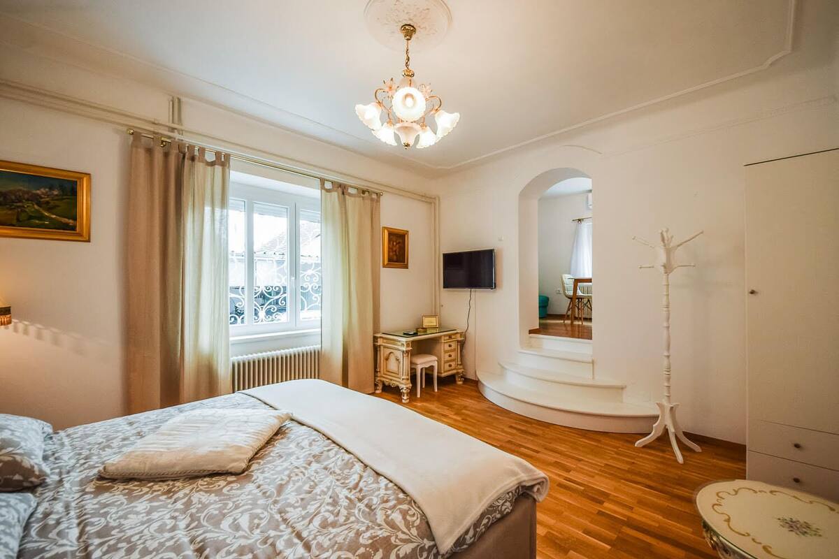 Een slaapkamer met een groot bed, een bureau, een stoel, een kapstok en een televisie.