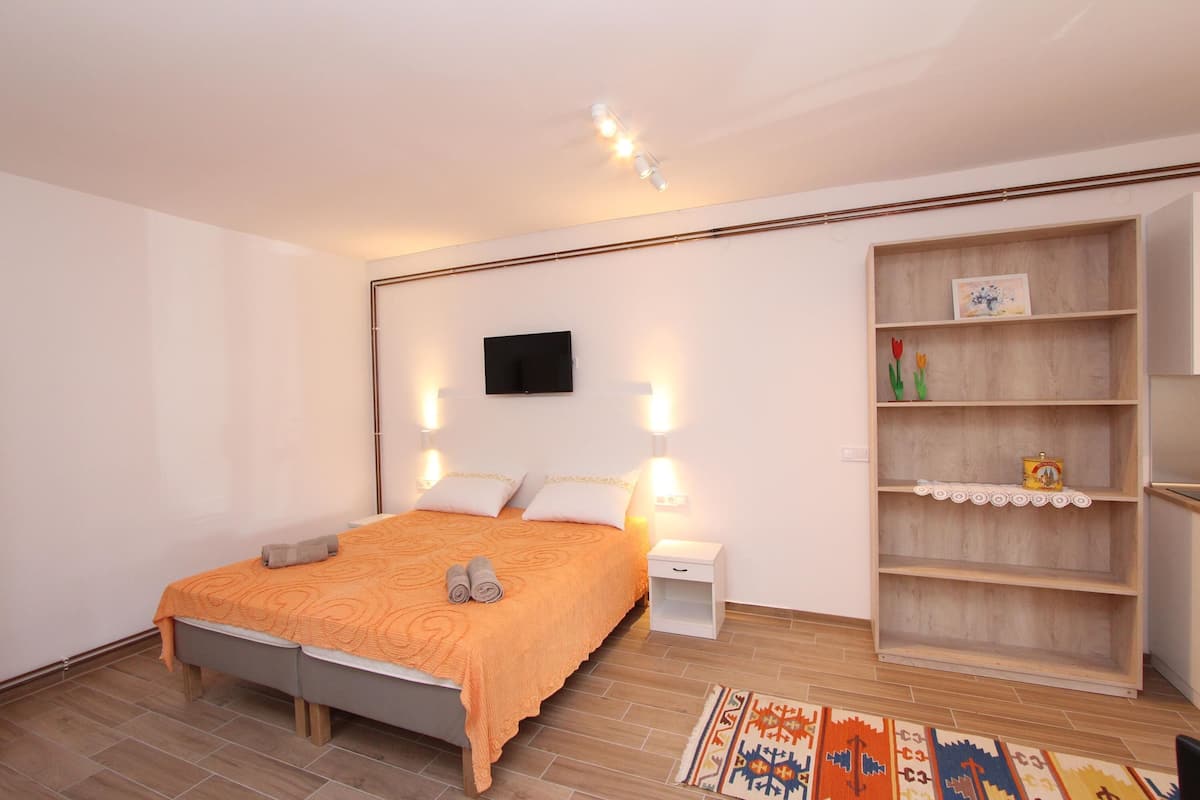 A bedroom with a bed, bedside tables, a TV, and a wooden shelf unit.