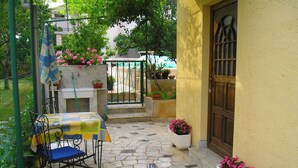 Un patio con piso de baldosas, una mesa y una silla azul, y plantas en macetas.