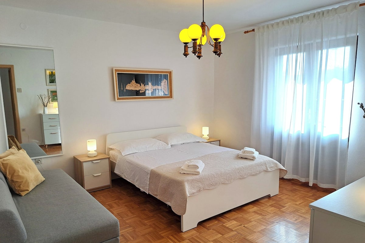 A neatly arranged bedroom with a bed, bedside tables, a lamp, and a mirror.